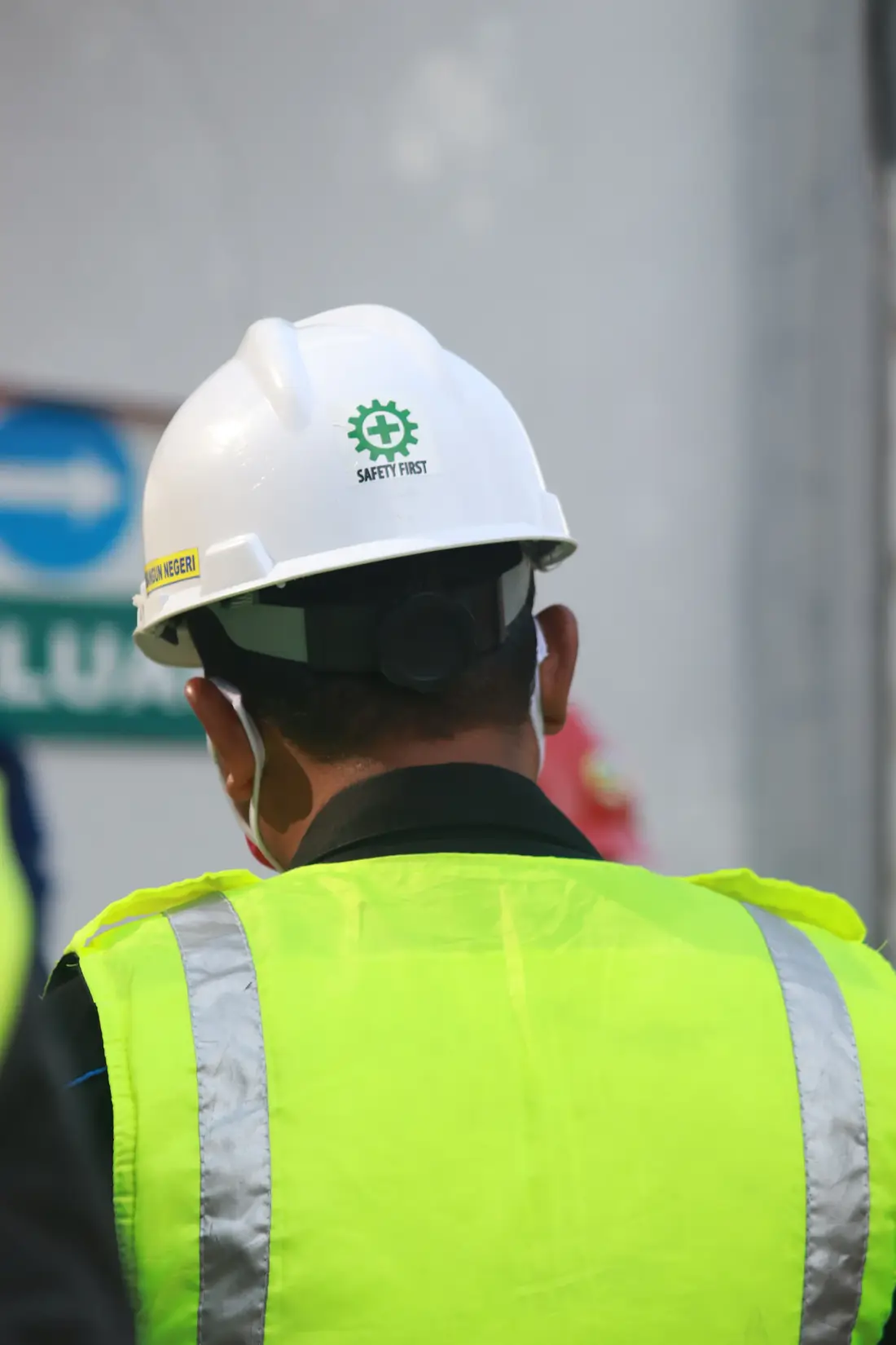 Trabajador de espaldas con casco blanco de seguridad y chaleco reflectivo en un frente de trabajo